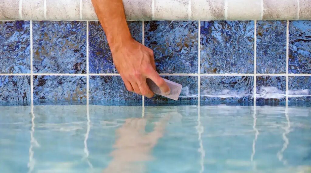 Technician removing calcium buildup from pool tile during calcium removal service in Dallas TX